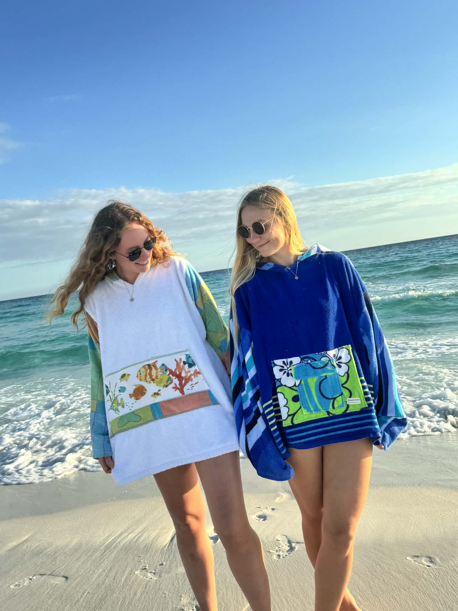 Two people on a beach wearing colorful hoodies with cartoon designs.